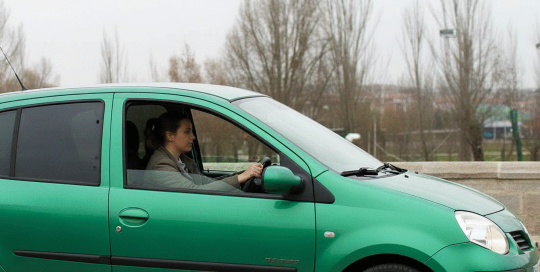 Mujer joven conduciendo un Renault Twingo verde con lunas tintadas traseras por un puente histórico de piedra en León, España, en un día nublado de otoño. Ideal para amantes de los coches urbanos y el turismo cultural en León