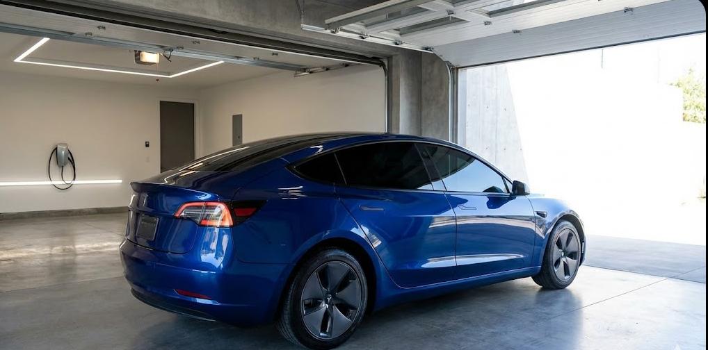 Coche eléctrico azul con lunas tintadas estacionado en un garaje moderno, imagen que representa el mantenimiento del vehículo y la protección del tintado cuando el coche duerme en garaje.